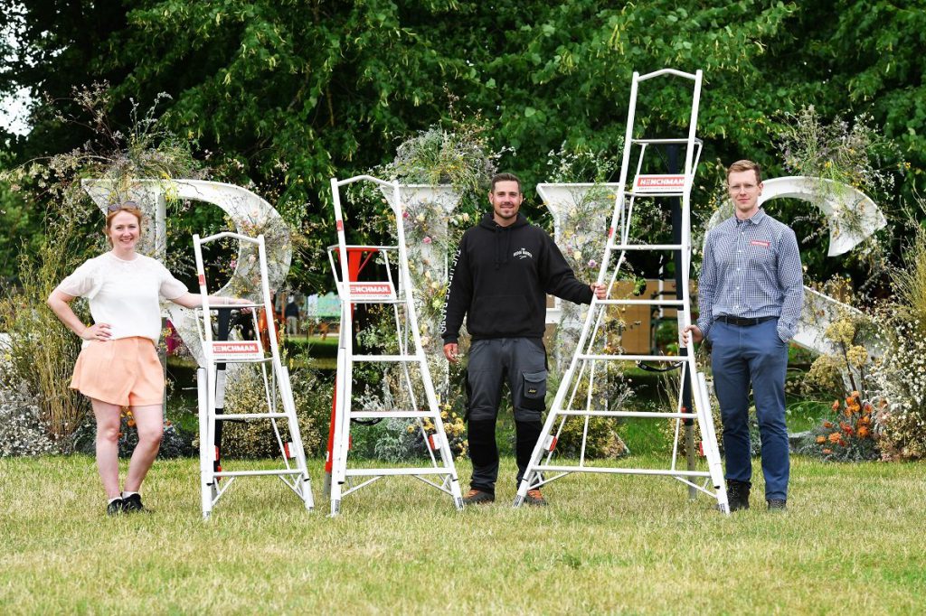 A group of three people holding metal ladders in front of a floral RHS sign
