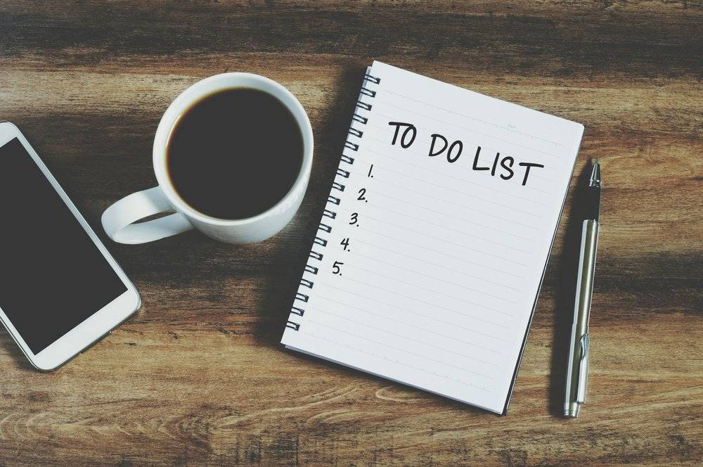 A notebook with a 'to do list' with a coffee and iphone on a wooden desk