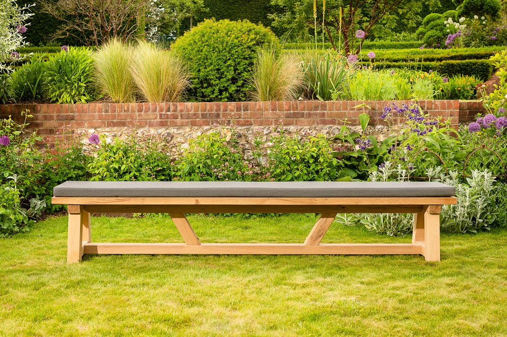A cushioned garden wooden bench on a grassy lawn area, with a garden scene in the background