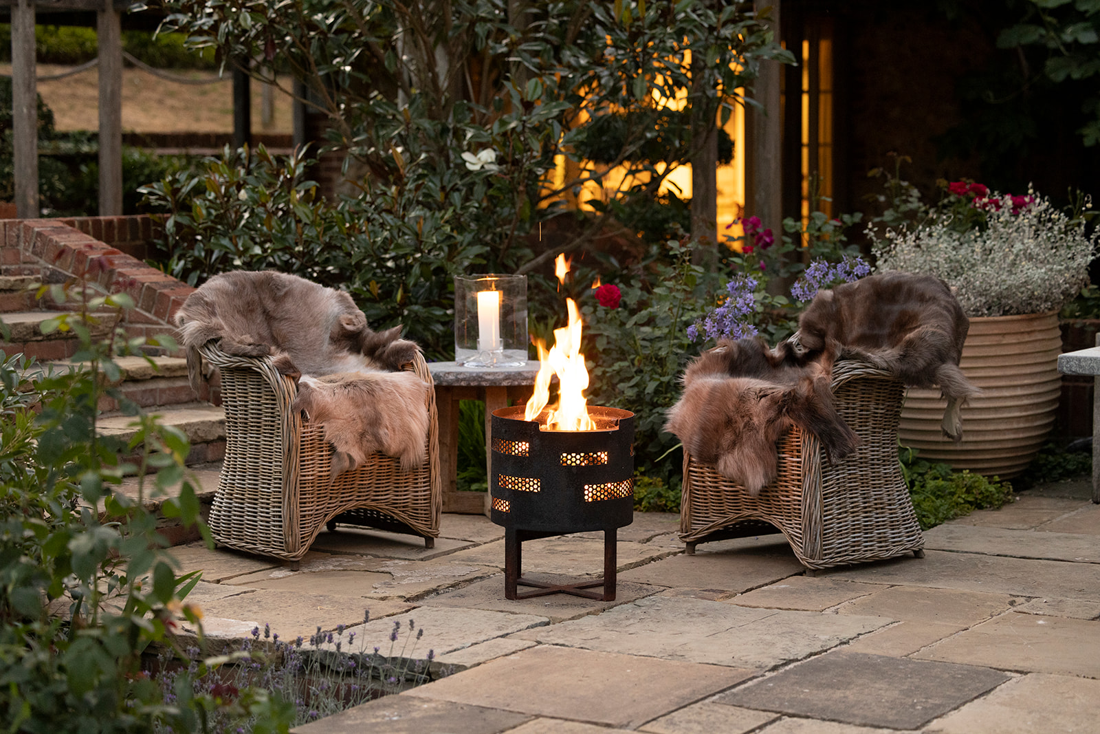 Two woven garden chairs surrounding a black fire basket on a patio area