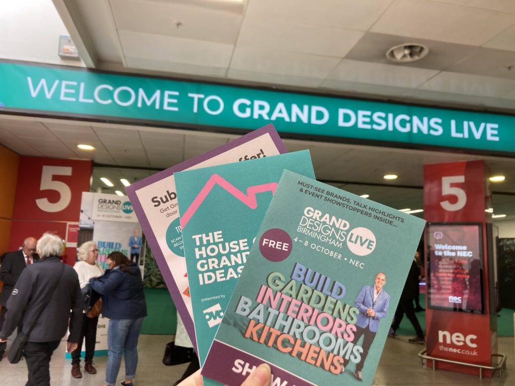 a person holding brochures in front of a sign saying 'welcome to grand designs live'