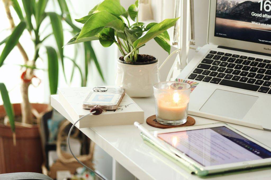 A desk with laptop, phone, lit candle and ipad