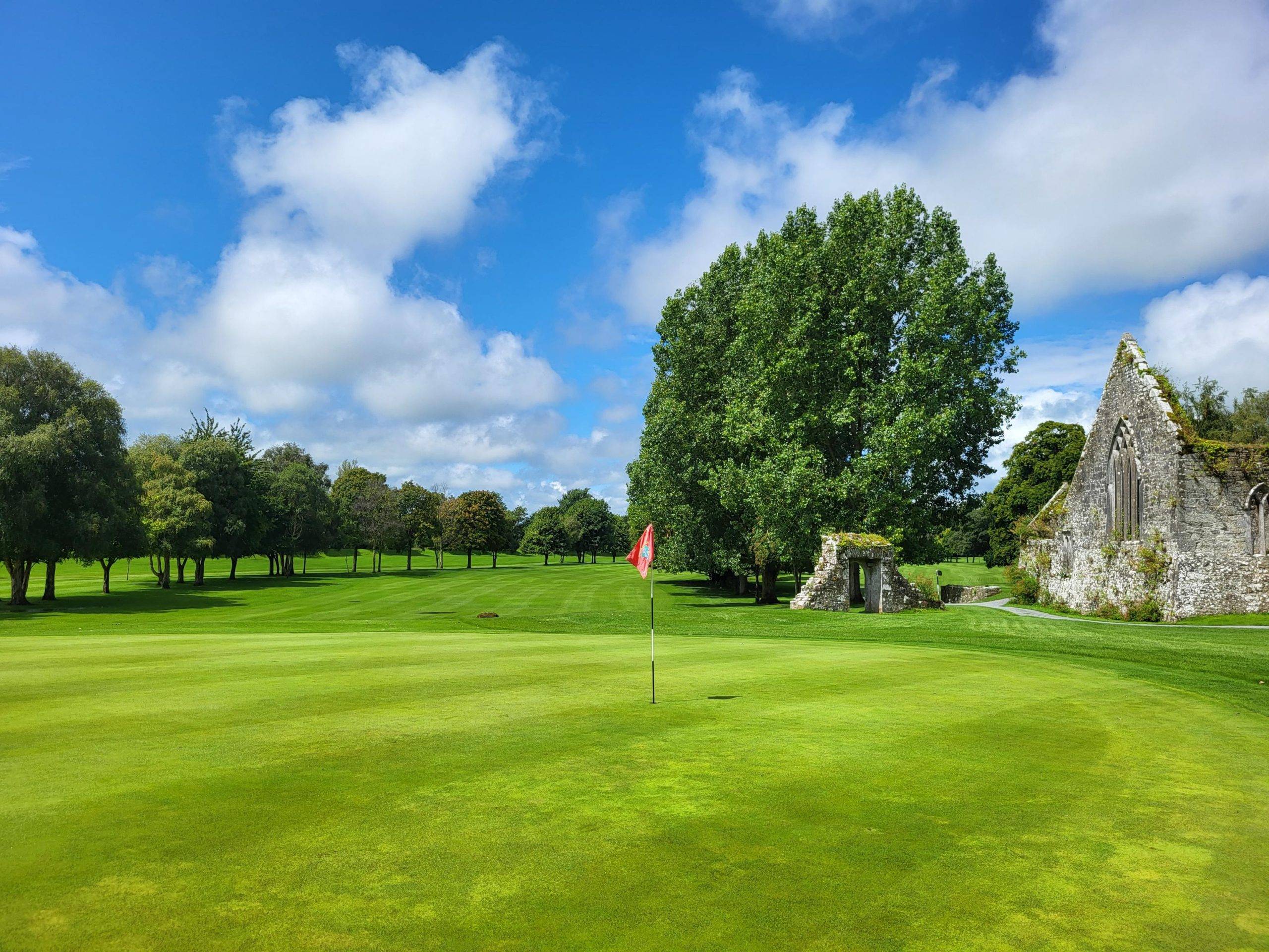 a manicured lawn at a golf course with ruins in the background