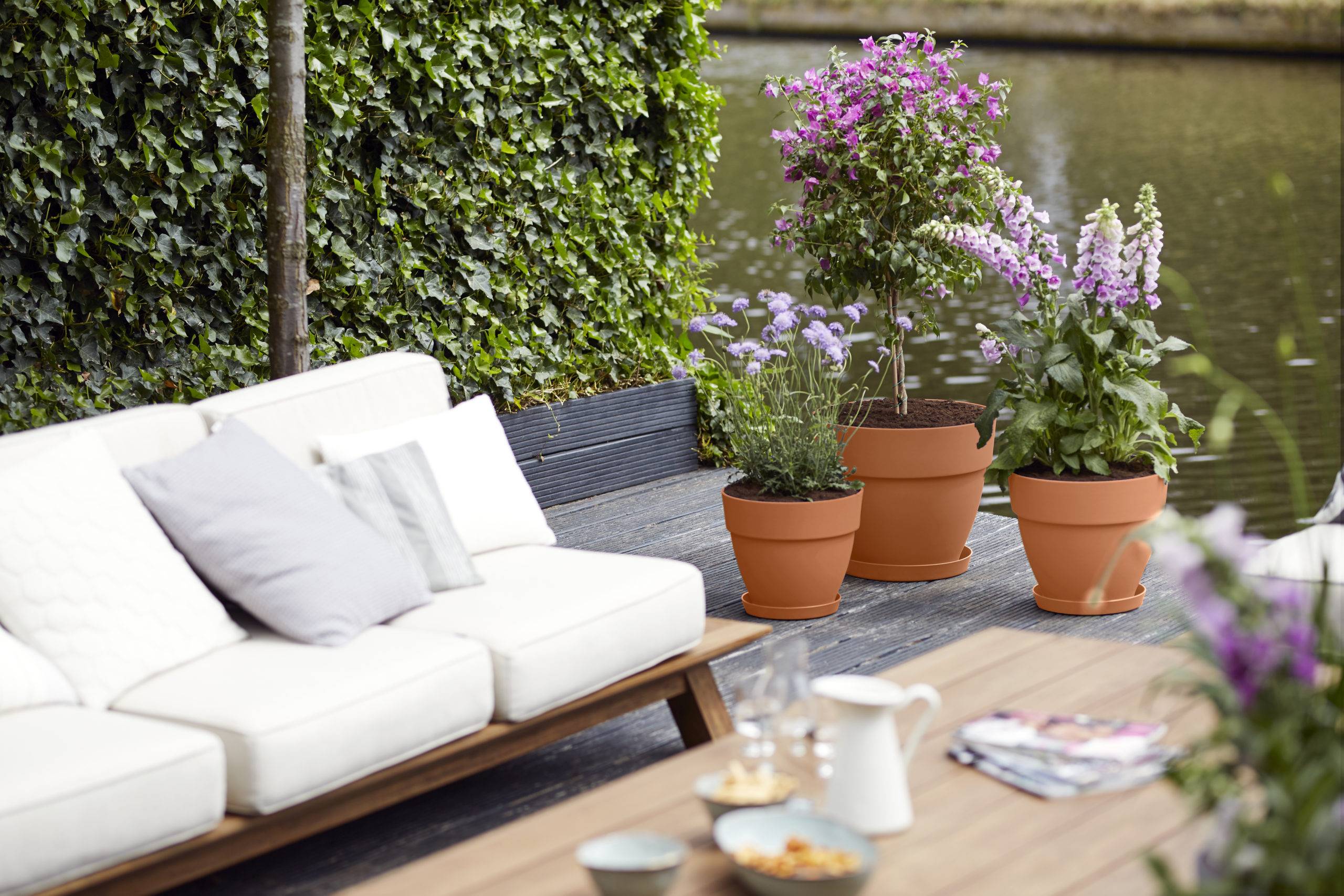 a garden seating area beside a river with orange planters with floral displays