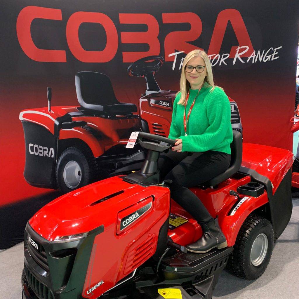 a woman sat on a bright red COBRA tractor in front of a display stand