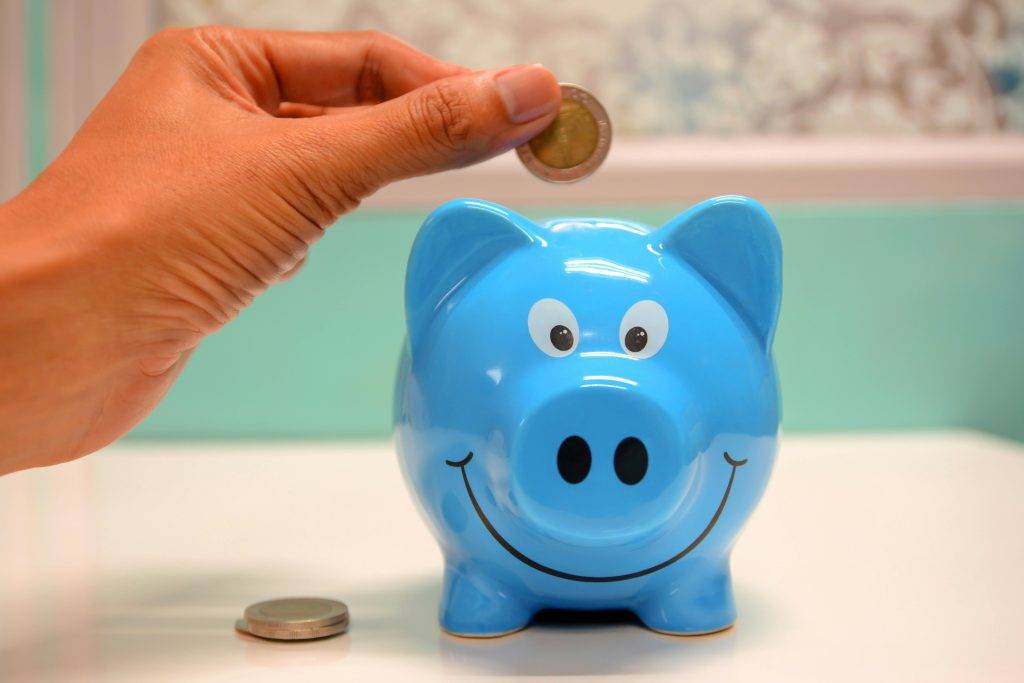 A person putting a pound coin into a blue piggy bank